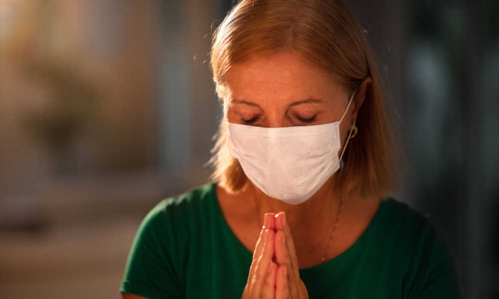A nurse in a face mask prays