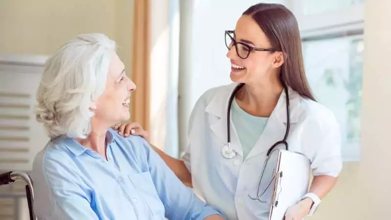 A nurse wearing a stethoscope smiles at a patient.