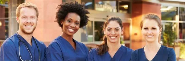 Four nurses in blue scrubs smile at the camera.