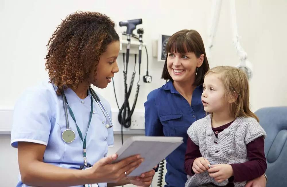 A family nurse practitioner speaks to a young patient and her parent.