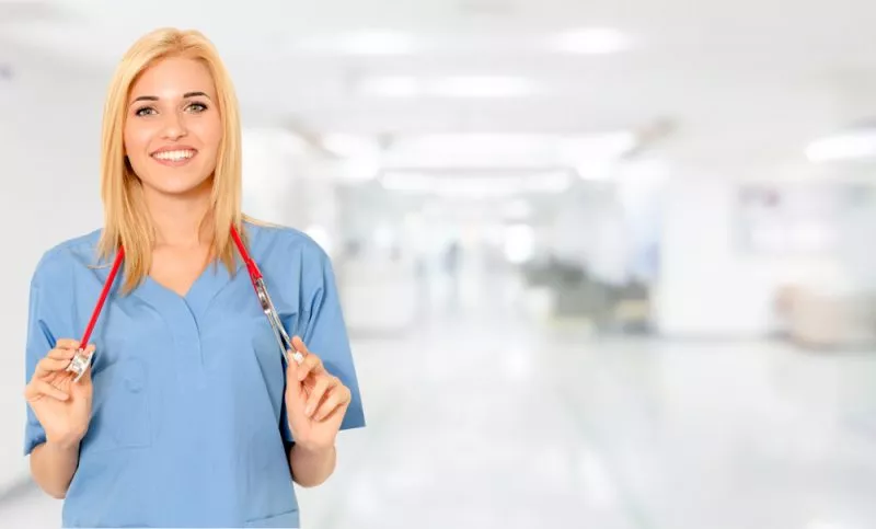 A nurse wearing scrubs and a stethoscope smiles at the camera.