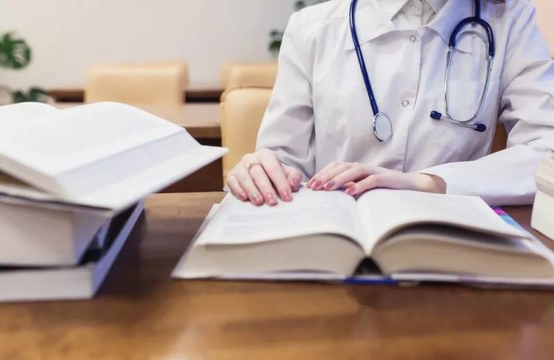 A closeup of a nursing student's hands reading an open book with stacks of books beside her.