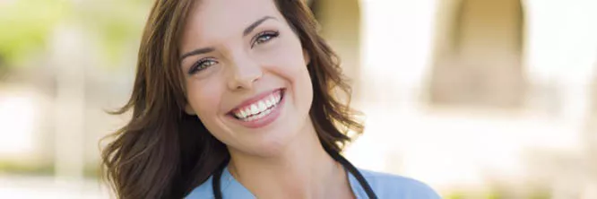 A nurse wearing scrubs and a stethoscope smiles at the camera.