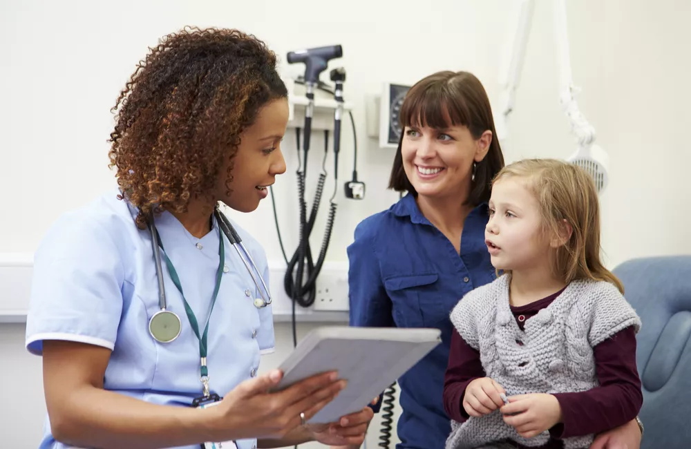 A nurse speaks to a young patient who is seated beside her mother.