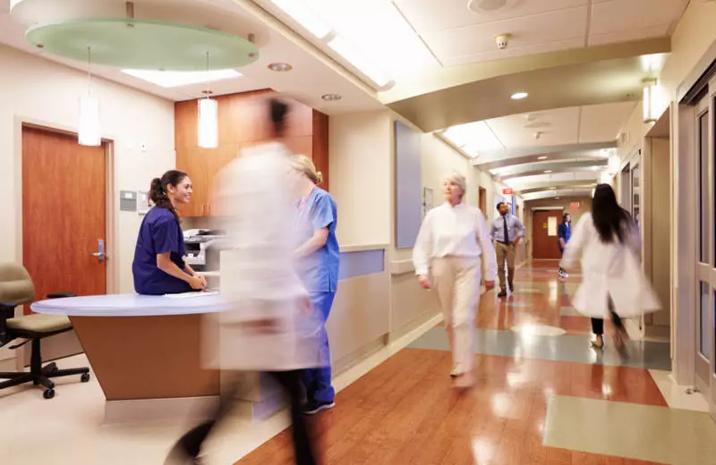 Multiple health care professionals pass each other in the hallway of a healthcare facility.