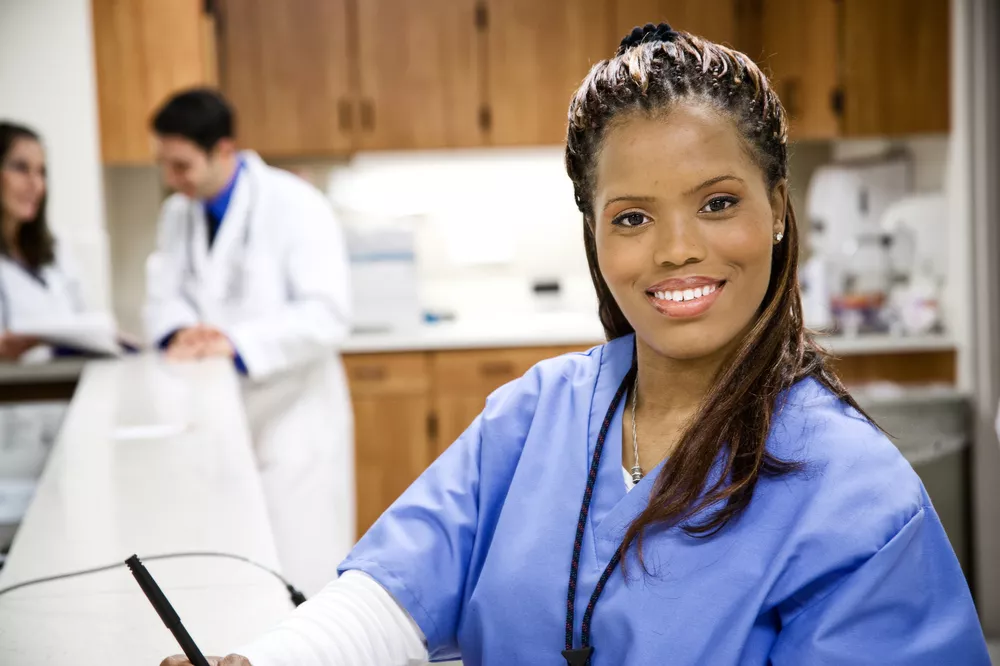 A nurse in scrubs smiles at the camera.