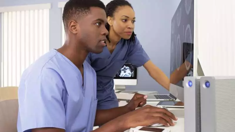 Two nurses work on computers and study the information on the screen.