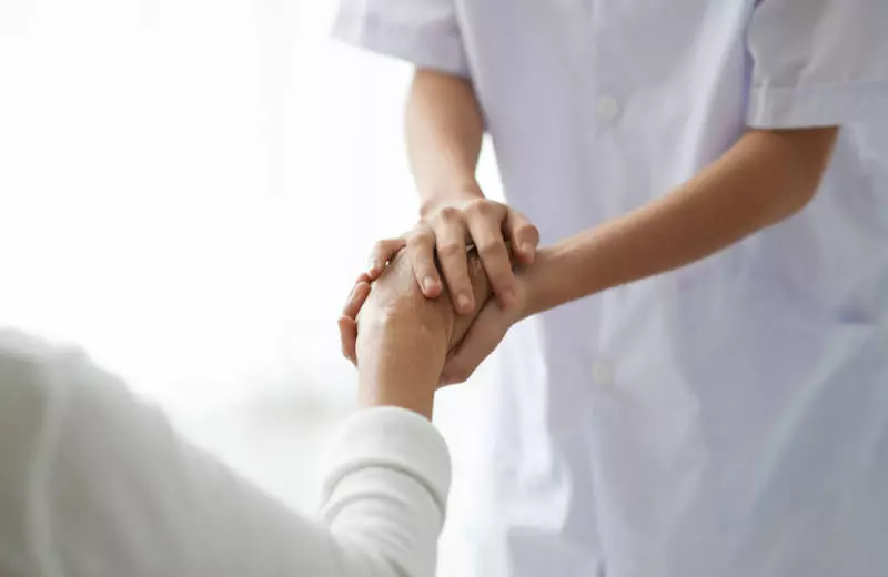 A nurse holds a patient's hand.
