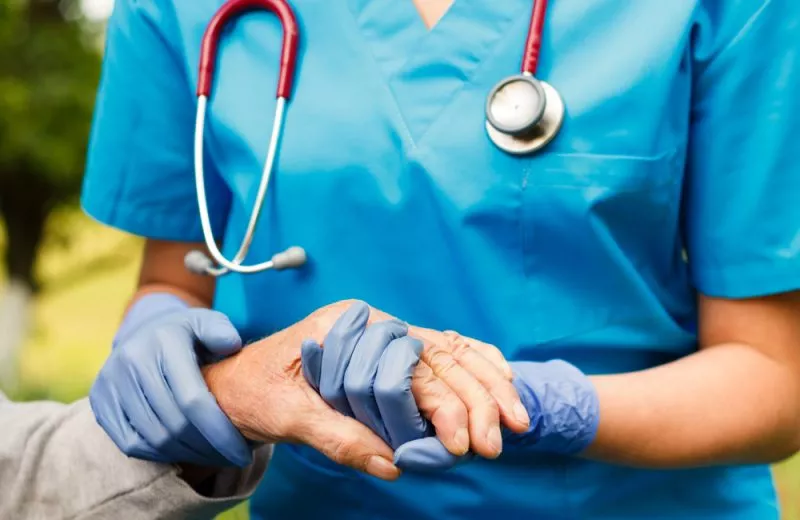 A closeup of a nurse's hands holding the hand of an older patient.