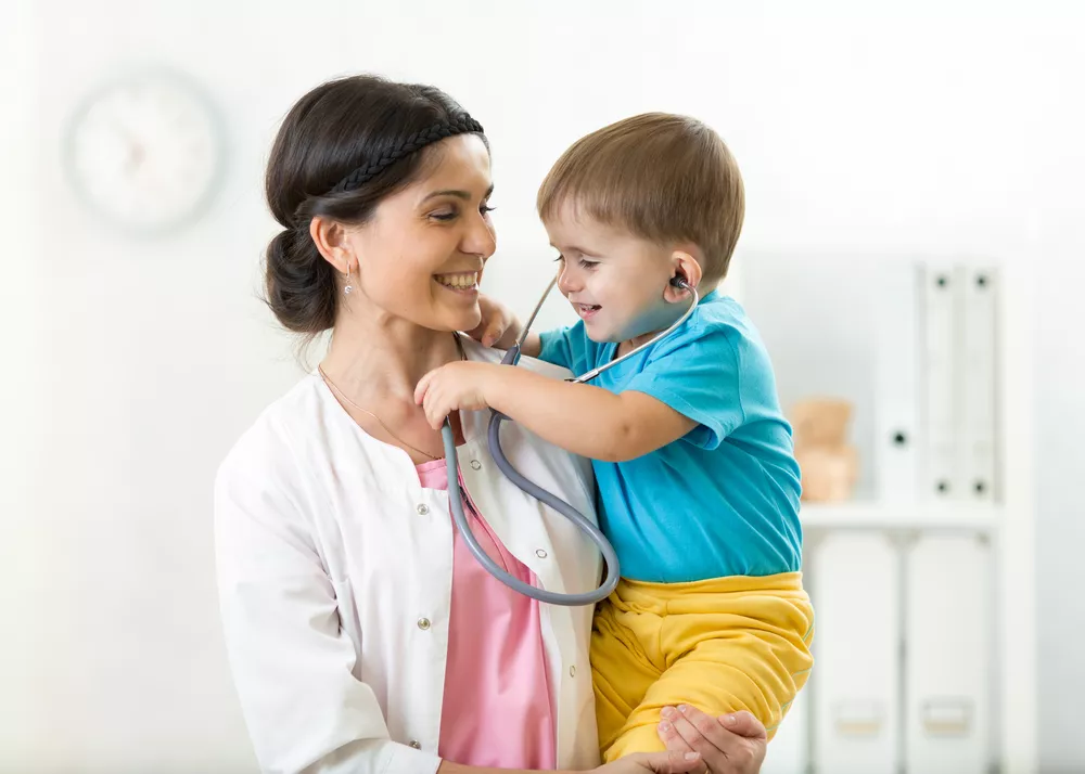 A nurse holds a young patient who plays with her stethoscope.