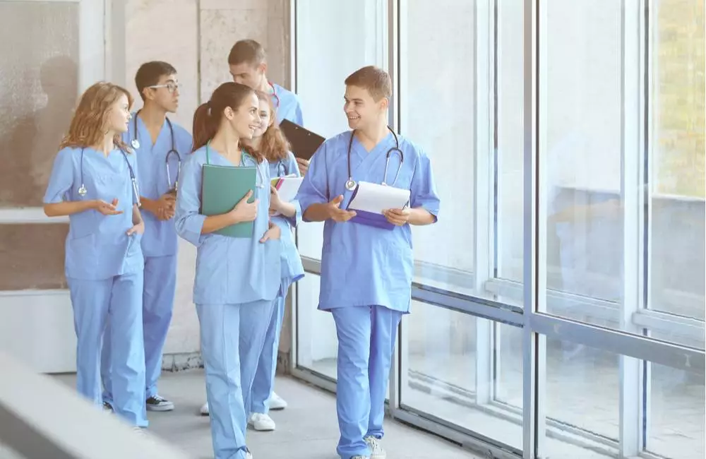 A group of nurses in scrubs walk down a hallway in conversation with each other.