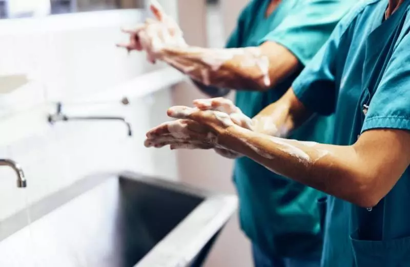 A closeup of several nurses washing their hands in a sink.