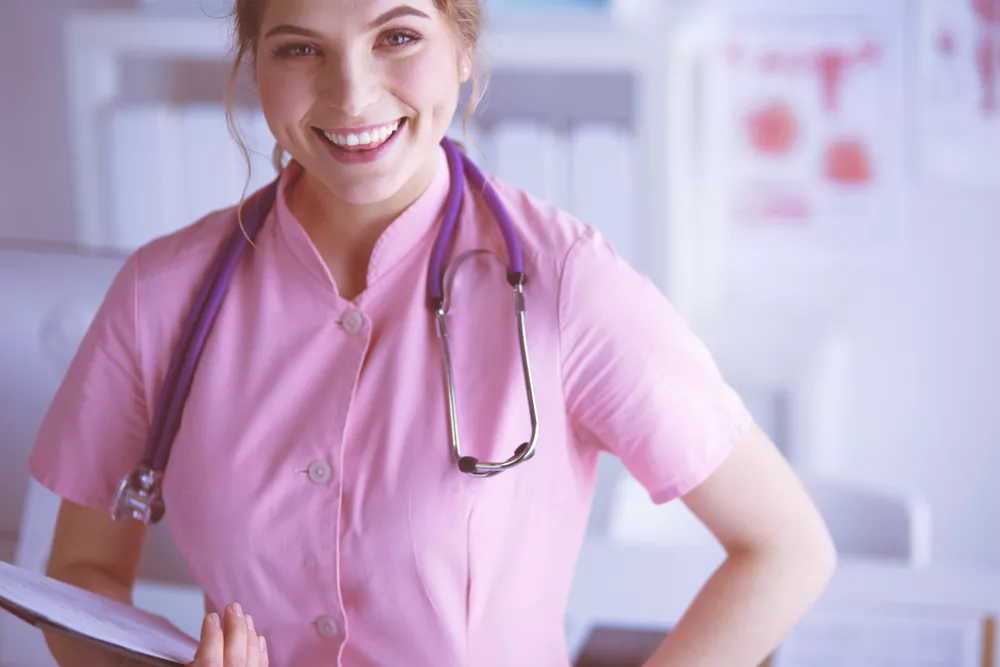 A nurse practitioner wears a stethoscope and holds a clipboard while smiling at the camera.