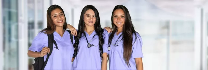 Three nurses in scrubs smile at the camera.