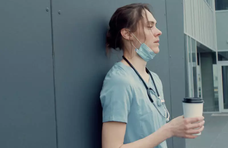 A nurse on a break leans against a wall with her eyes closed.