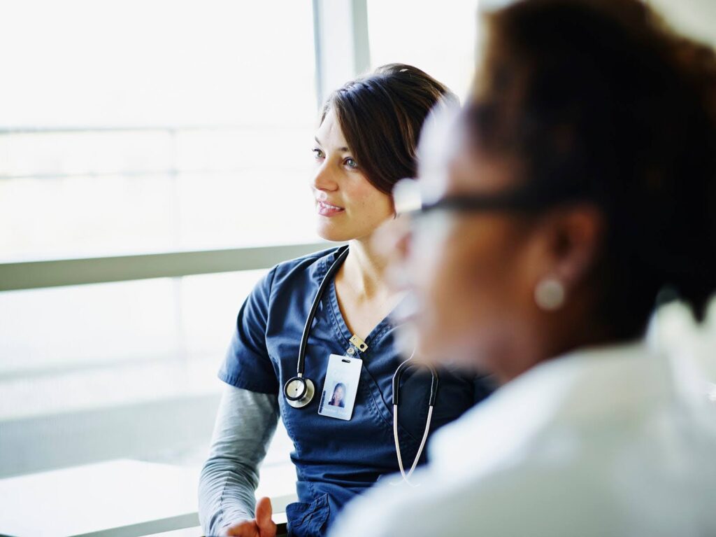 Two female nurses listen attentively during a medical meeting.