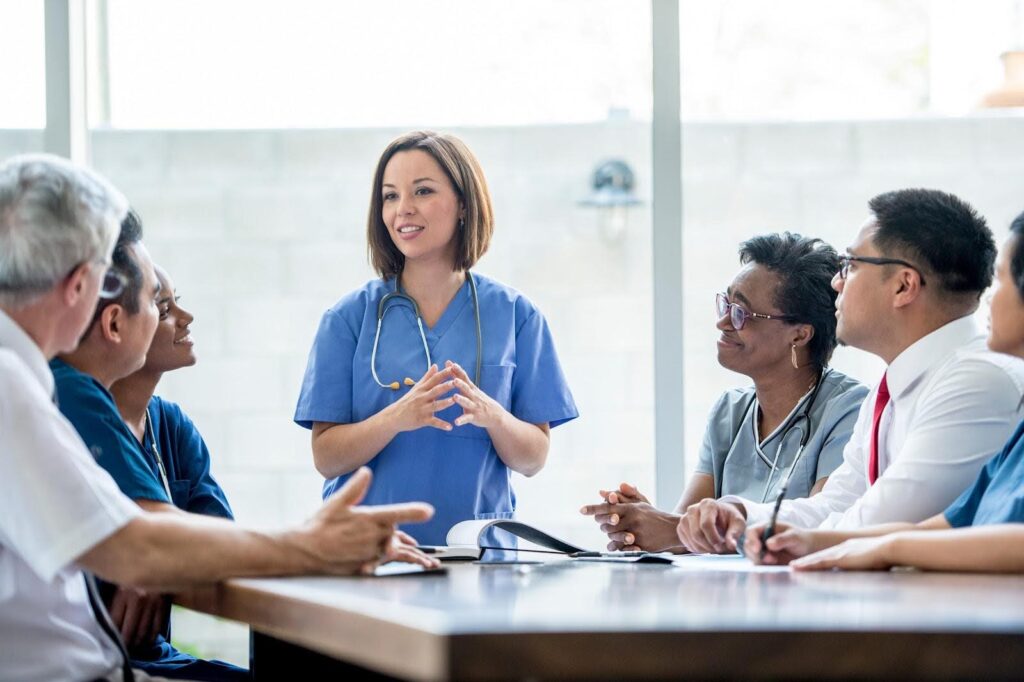 A nurse addresses nursing colleagues at a conference table.